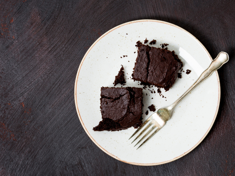 Prato branco com dois pedaços de bolo de chocolate em cima, acompanhados de um garfo ao lado do bolo
