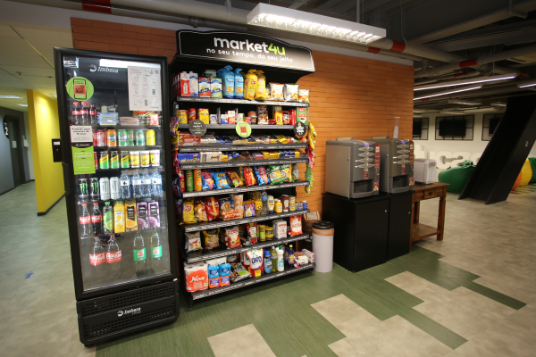 Uma geladeira e uma gôndola do market4u, instaladas em uma empresa, com produtos para o dia a dia, como refrigerantes, salgadinhos, pães e muitos outros.