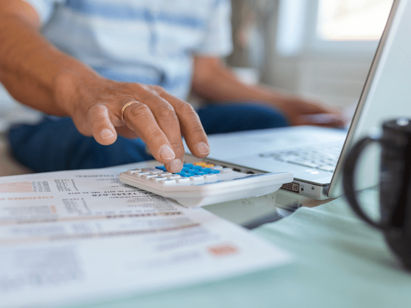 Homem sentado em frente ao computador mexe na calculadora enquanto declara seu imposto de renda