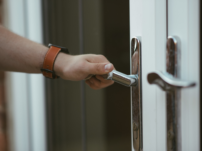 A mão de um homem branco segura uma maçaneta, como se fosse abrir a porta, para indicar furto no condomínio