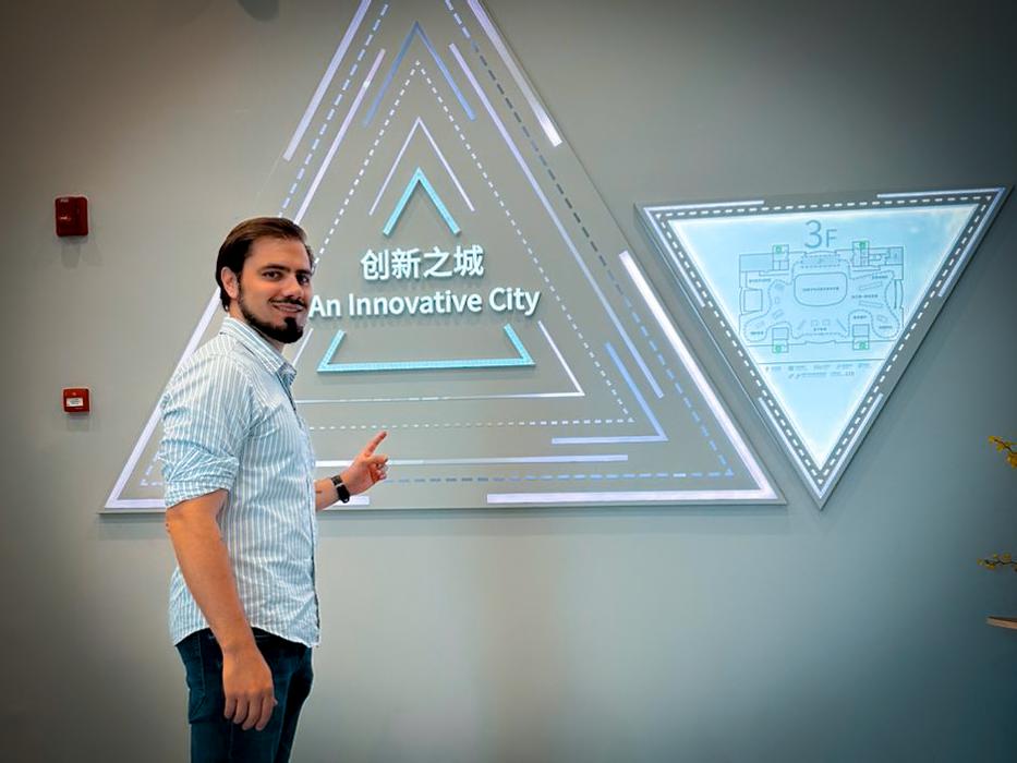 Eduardo Cordova, CEO do market4u, em viagem à China, posa em frente a uma parede e aponta para uma pirâmide