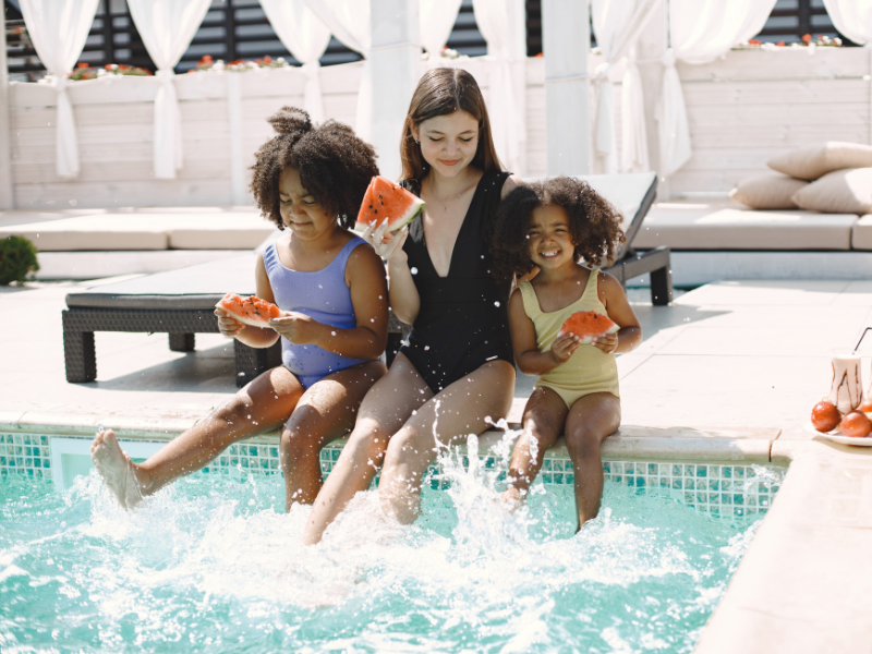 Três crianças, uma ao lado da outra na piscina, passando as férias no condomínio