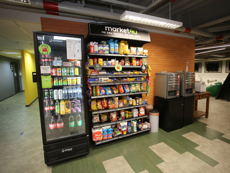 Uma geladeira e uma gôndola de supermercado instaladas em um subsolo exemplificando um mercadinho na empresa