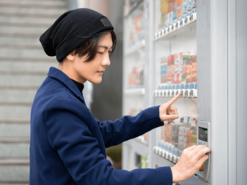Homem oriental abrindo uma máquina de venda automática para retirar produtos